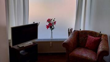 Ett vardagsrum med en soffa, en tv, ett element och ett fönster med gardiner.