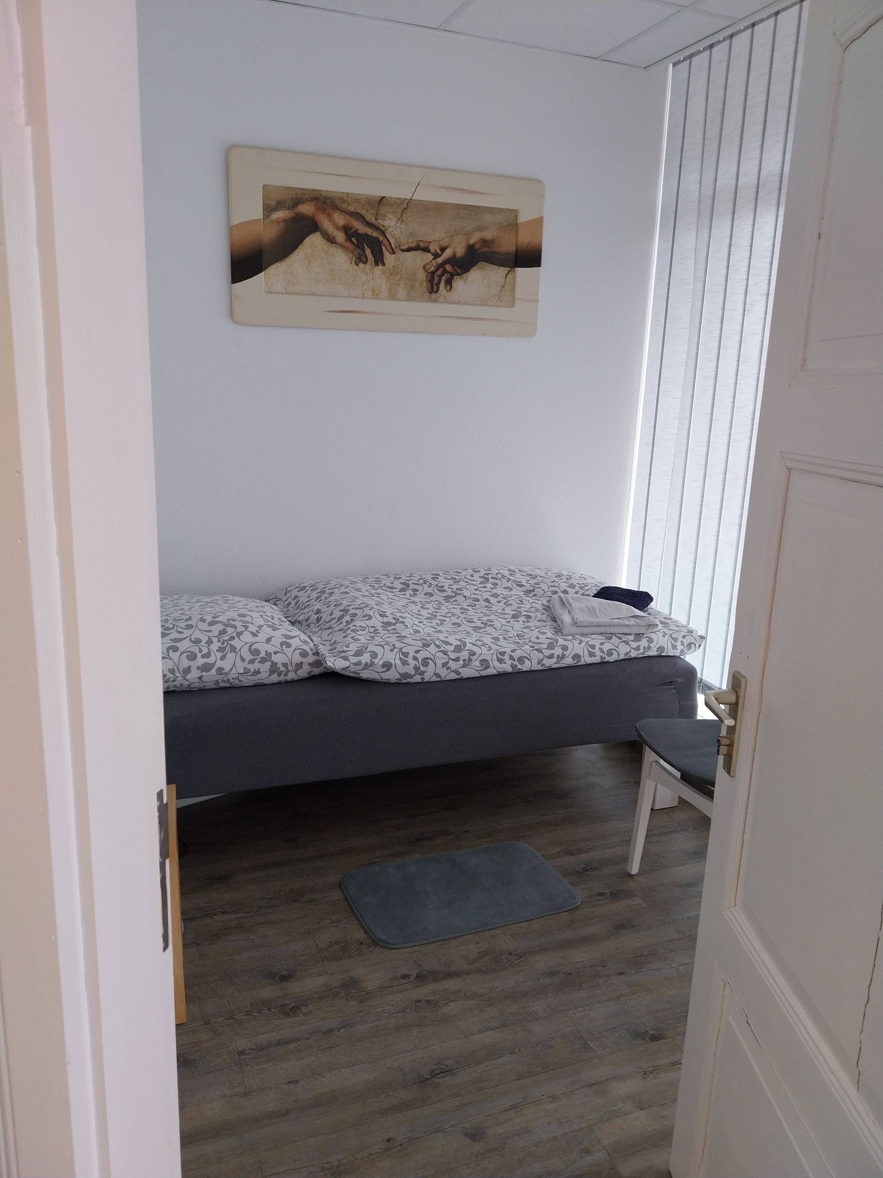 A room with a bed, a bench, a door, and a wall-mounted picture.
