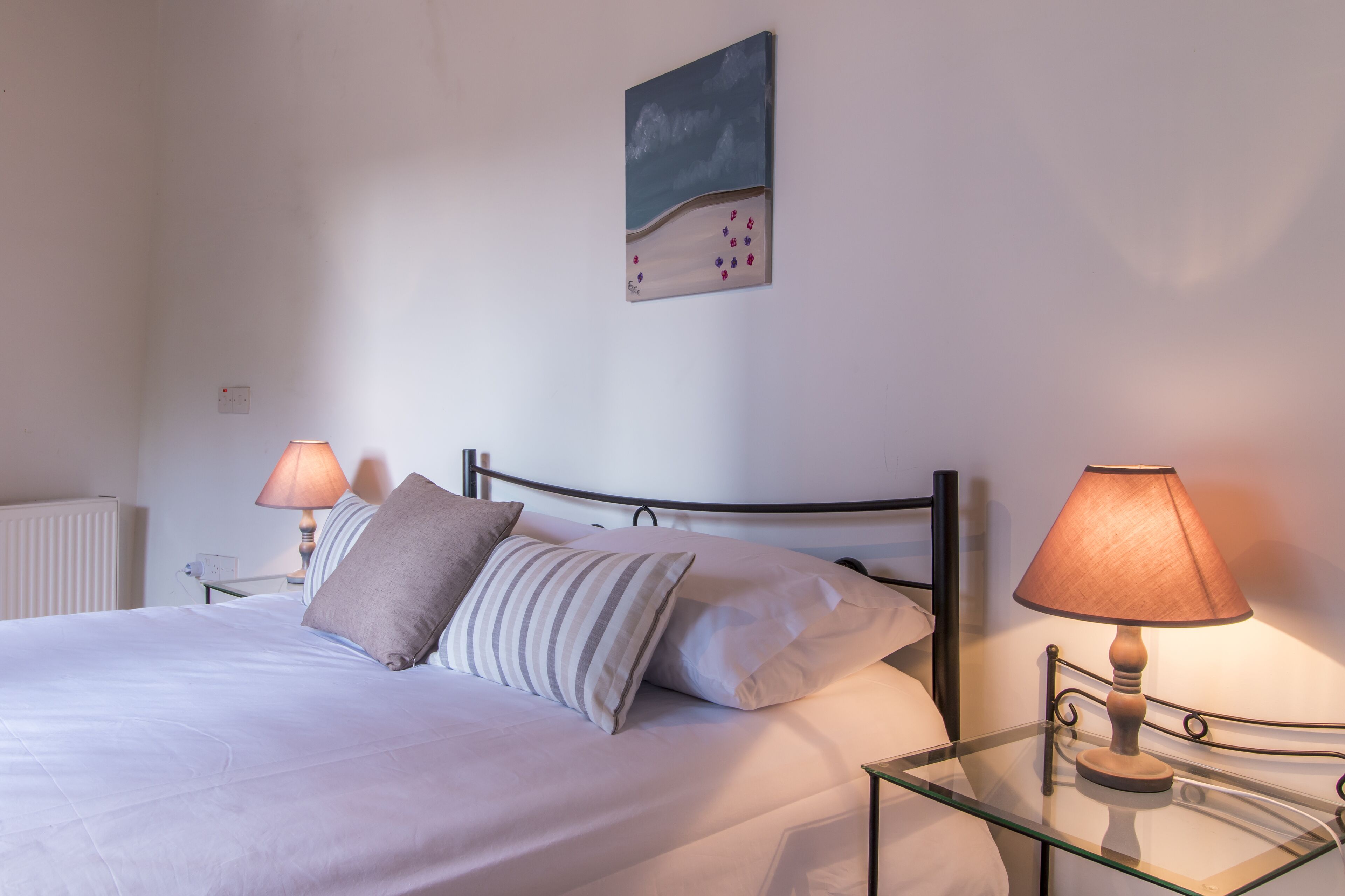 A neatly made bed with pillows, a bedside table with a lamp, and a painting on the wall.