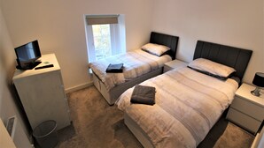Une chambre avec deux lits, un bureau avec un ordinateur et une fenêtre.