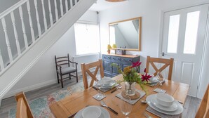 Un coin repas avec une table en bois dressée pour quatre personnes, un vase rempli de fleurs et un miroir au-dessus de la table.
