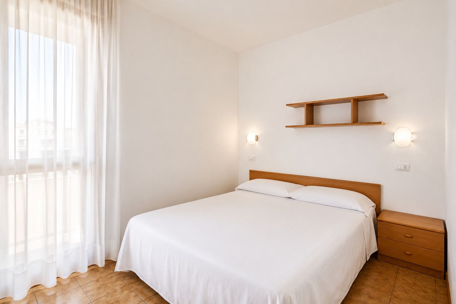 A bedroom with a bed, a nightstand, a wall-mounted shelf, and two wall sconces.