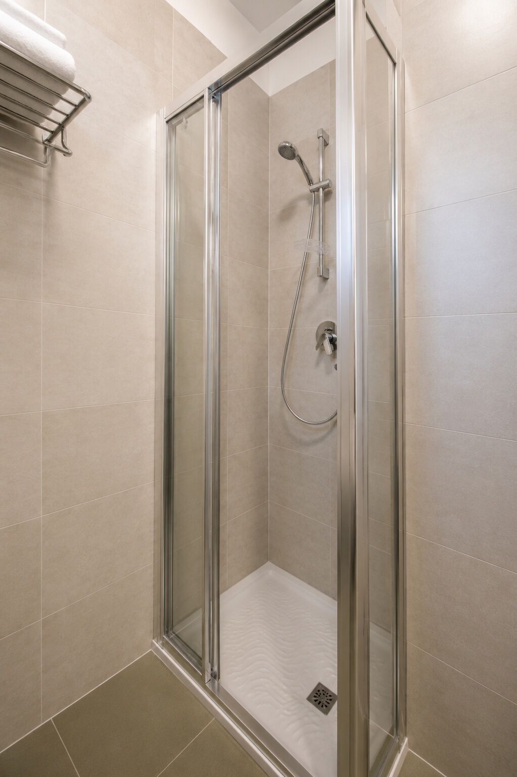 A glass-enclosed shower stall with a handheld showerhead and a wall-mounted faucet.