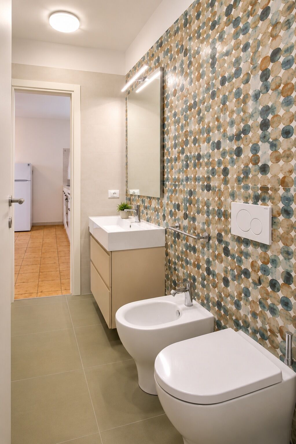 Une salle de bain avec deux toilettes, un lavabo, un miroir et un mur décoré d’un motif.