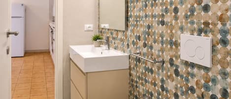 A bathroom with two toilets, a sink, a mirror, and a patterned wall.