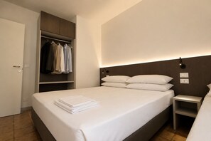 Une chambre d’hôtel comprenant un lit, une table de chevet, une armoire et une lampe fixée au mur.