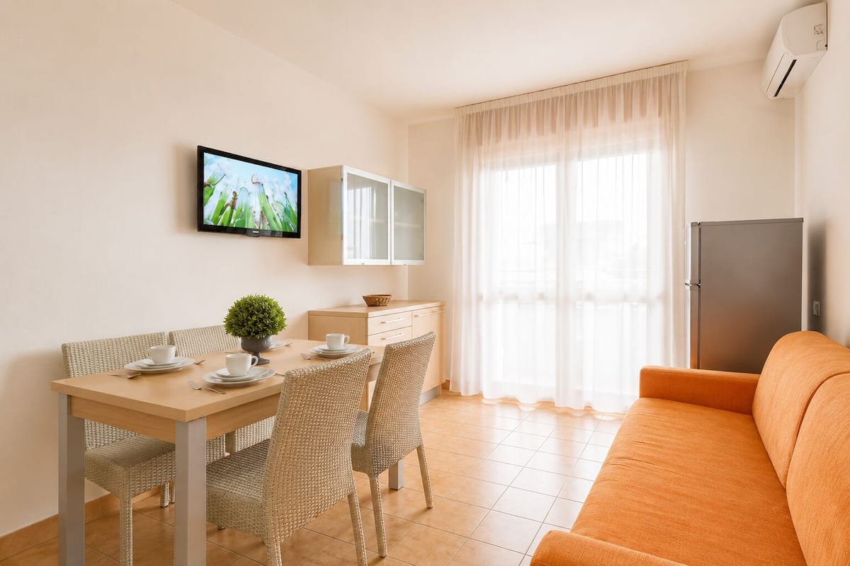 Ein modernes Wohnzimmer mit Essbereich, einem an der Wand montierten Fernseher, einem Kühlschrank und einem Sofa.