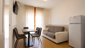 A modern living room with a dining table, chairs, a sofa, and a refrigerator. - Residence Columbia (San Michele al Tagliamento)