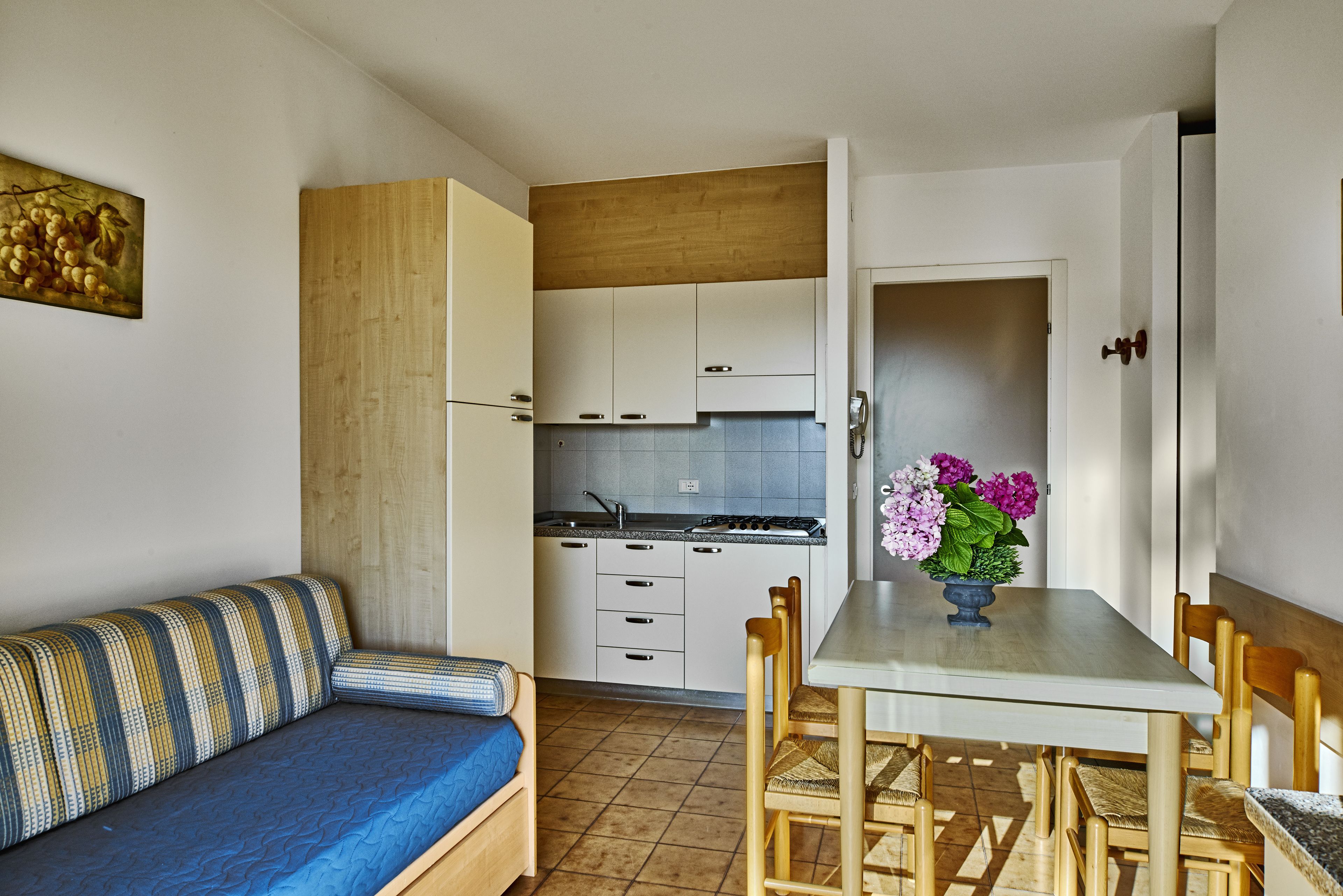 Cocina compacta con armarios blancos, una mesa de comedor con sillas y un sofá azul.