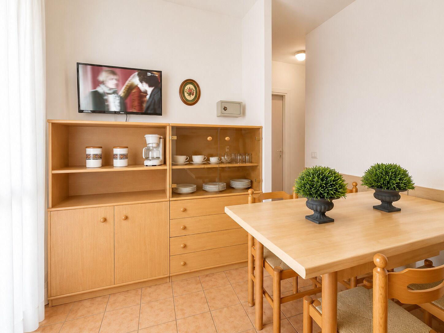 A compact kitchen with wooden cabinets, a coffee maker, and a TV mounted above the counter.