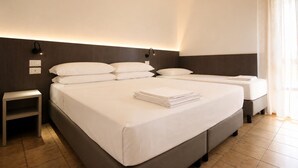 A hotel room with a large bed, a smaller bed, a nightstand, and a wall-mounted light fixture. - Residence Columbia (San Michele al Tagliamento)