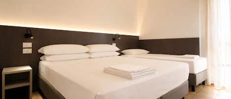 A hotel room with a large bed, a smaller bed, a nightstand, and a wall-mounted light fixture.