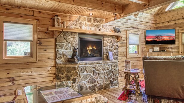 Interior acogedor de una cabaña con chimenea de piedra, paredes de madera, un televisor y una mesa de vidrio con un menú.