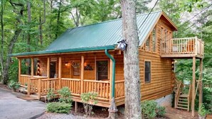 Eine Holzhütte mit einem grünen Dach, einer Veranda und einem kleinen Balkon.