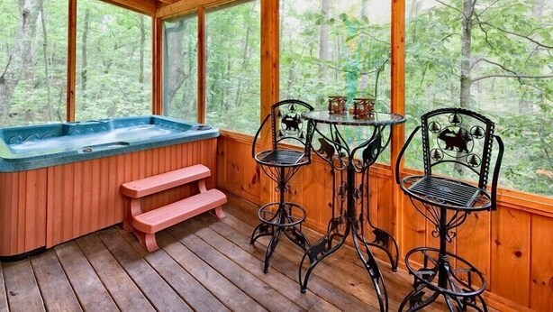 Eine Holzterrasse mit einem Whirlpool, zwei Metallstühlen und einem kleinen Tisch.