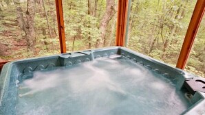 Ein Whirlpool mit Blick auf einen Wald durch große Fenster.