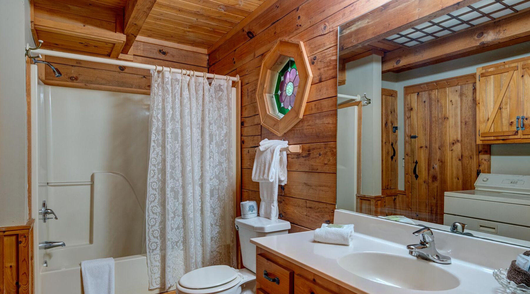 A wooden cabin bathroom with a shower, toilet, sink, and a large mirror.