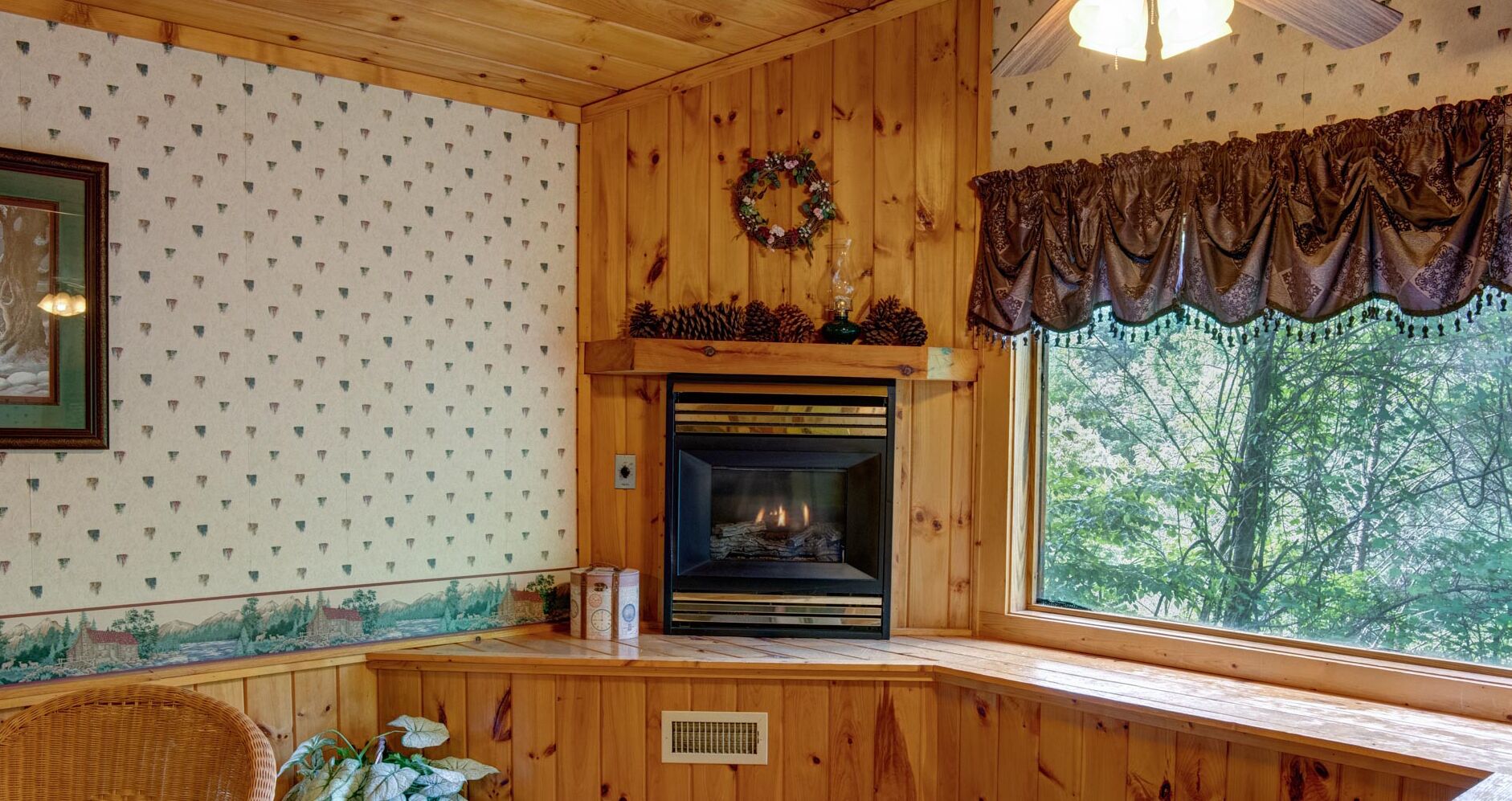 Una stanza accogliente con camino, pareti in legno, una finestra vista alberi e un ghirlanda decorativa sopra il camino.