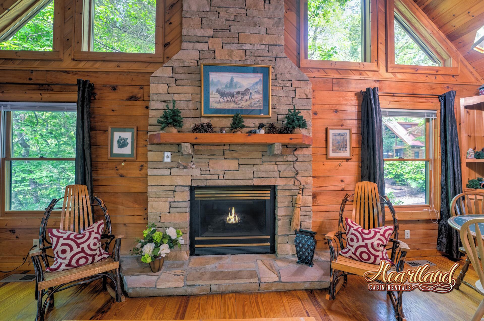 A cabin with a stone fireplace, wooden walls, and large windows.
