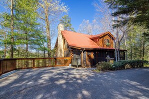 A log cabin with a chimney, surrounded by a wooden fence, and a paved driveway leading to the entrance.