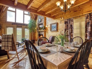 A wooden interior with a dining table set for four, a fireplace, and a clock on the wall.