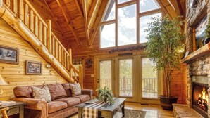 A log cabin interior with a wooden staircase, a fireplace, a leather sofa, and a dining table. - Sweet Dreams is a beautiful 2 bedroom and 2 bath log cabin (Sevierville)