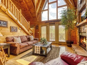 A log cabin interior with a wooden staircase, a fireplace, a leather sofa, and a dining table.