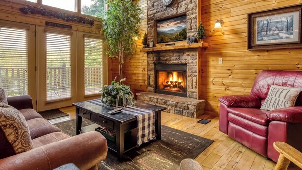 A cozy living room with a fireplace, wooden walls, a large window, and a red leather sofa. - Sweet Dreams is a beautiful 2 bedroom and 2 bath log cabin (Sevierville)
