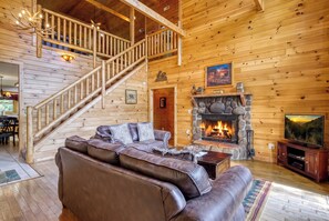 A log cabin interior with a stone fireplace, leather sofa, wooden staircase, and a television. - Amazing Views - The name says it all! (Sevierville)