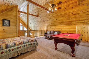 A cozy room with a wooden ceiling, a pool table, a sofa, and a bed with a quilt.