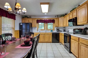 A kitchen with wooden cabinets, a refrigerator, a dishwasher, and a dining area with a table set for two. - Amazing Views - The name says it all! (Sevierville)