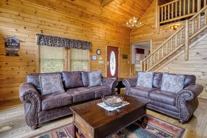 A cabin interior with two leather sofas, a wooden coffee table, a chandelier, a wooden staircase, and a cabin rules sign. - Amazing Views - The name says it all! (Sevierville)