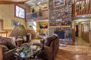 A spacious cabin interior with a stone fireplace, wooden furnishings, and a balcony with railings. - Diamond In The Rough, is a terrific family or group cabin. Pigeon Forge Cabin (Sevierville)
