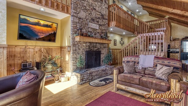 A cabin interior with a stone fireplace, wooden furniture, a mounted painting, and a staircase. - Diamond In The Rough, is a terrific family or group cabin. Pigeon Forge Cabin (Sevierville)