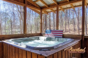 A wooden cabin with a hot tub, surrounded by a forest.