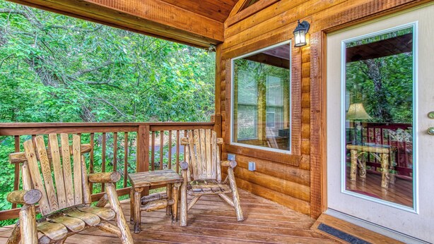 A wooden deck with a wooden chair and table, a glass door, and a view of greenery. - Above The Clouds is a perfect Smoky Mountain Getaway for the family or 2 couples! (Sevierville)