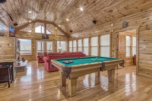 A wooden interior with a pool table, red sofa, and a fireplace.