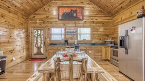 A wooden cabin interior with a kitchen featuring a wooden dining table, a refrigerator, and a bear warning sign. - Above The Clouds is a perfect Smoky Mountain Getaway for the family or 2 couples! (Sevierville)