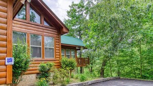 A log cabin with a porch, surrounded by lush greenery. - Above The Clouds is a perfect Smoky Mountain Getaway for the family or 2 couples! (Sevierville)