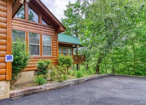A log cabin with a porch, surrounded by lush greenery.