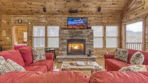 A cozy cabin interior with a stone fireplace, red couches, and a television mounted above it. - Above The Clouds is a perfect Smoky Mountain Getaway for the family or 2 couples! (Sevierville)
