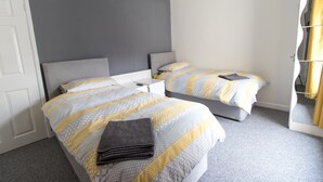 Quarto de hotel com duas camas, paredes cinzentas e uma porta branca.