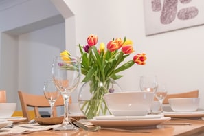 Taula de menjador preparada amb plats, bols i coberts blancs, juntament amb un ram de tulipes.