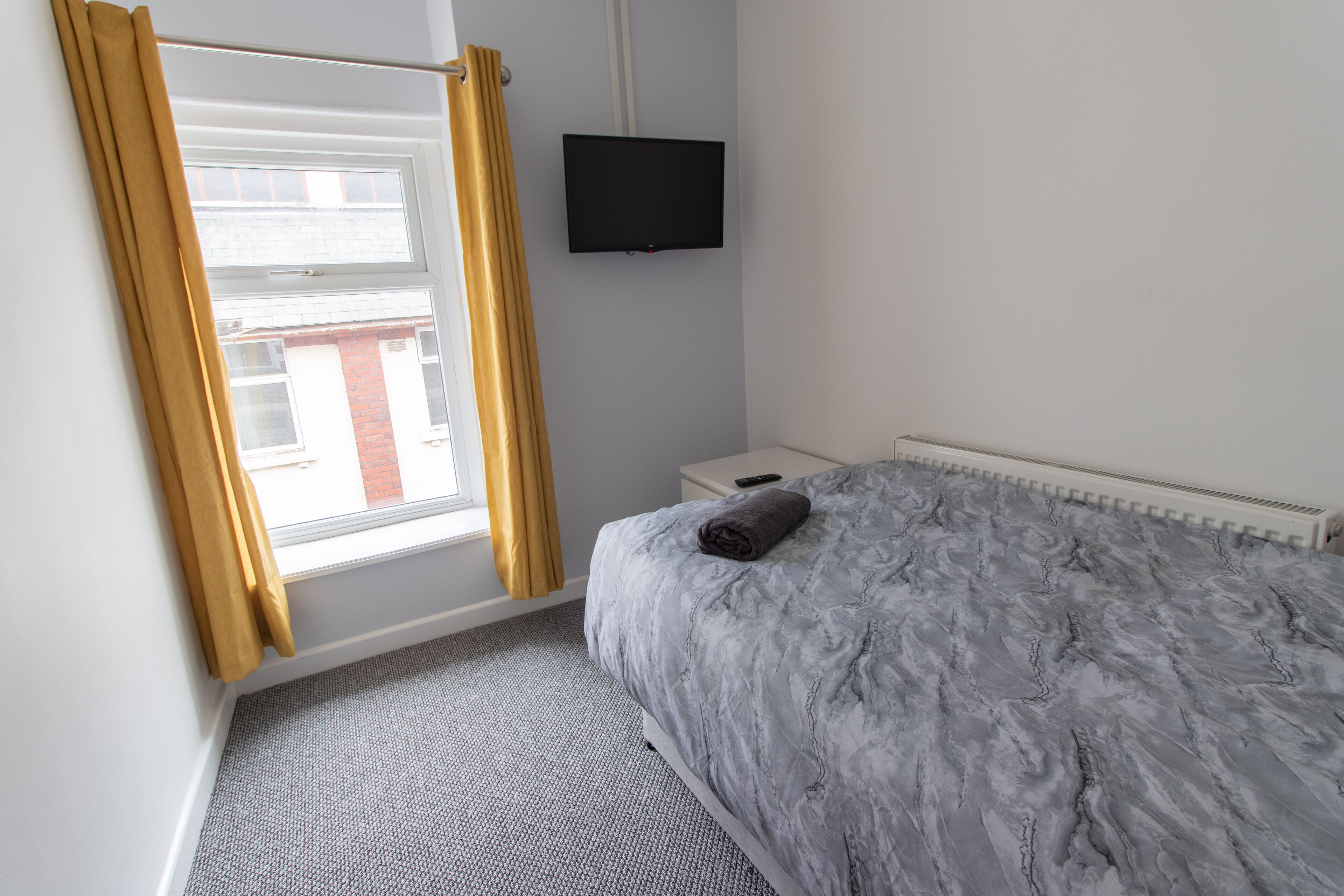 A bedroom with a bed, a TV mounted on the wall, and a window with curtains.