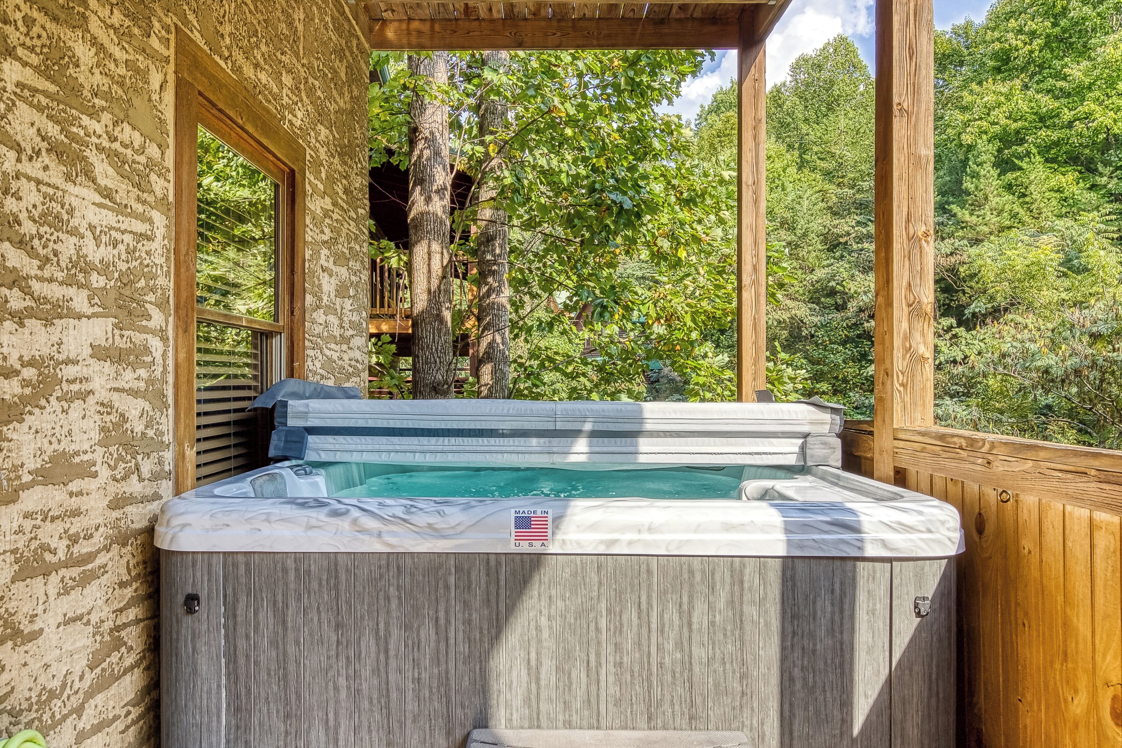Un jacuzzi en un área de terraza de madera con vistas a árboles y un muro de piedra.