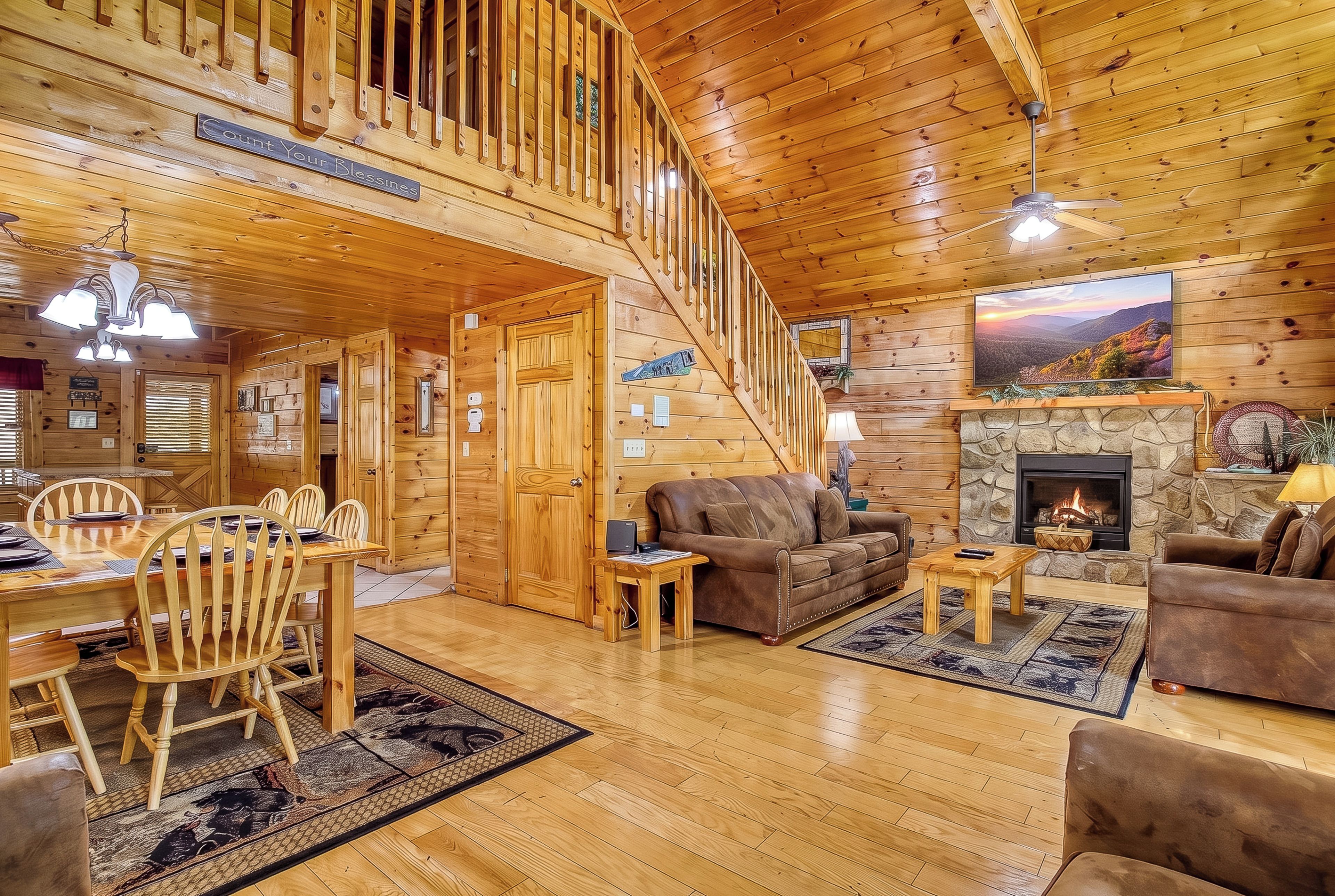 A spacious living area with a wooden staircase, a fireplace, and a dining area with wooden furniture.