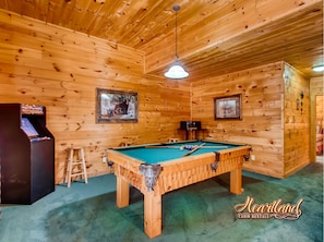 Relax in this cabin's spacious room, featuring a pool table, comfortable seating, and a mounted TV.