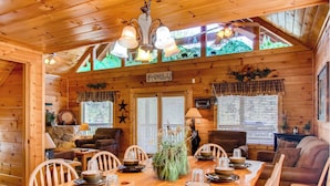 A cozy cabin interior with a wooden dining table set for four, surrounded by chairs. A sign on the wall reads "FAMILY".
