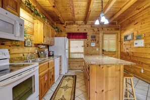 Innenansicht einer Holzhütte mit Küchenbereich, einschließlich Mikrowelle, Herd, Spüle und Kühlschrank.