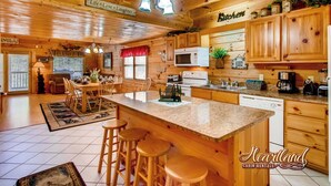 A cabin interior with a wooden interior, a kitchen with a microwave, stove, and sink, a dining area with chairs and a table, and a bar area with stools.
